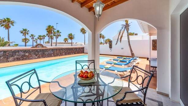 A poolside area with a glass table, chairs, and a fruit bowl. - Villa Nino by Villa Plus (Puerto del Carmen)