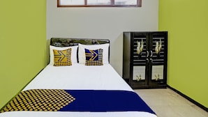 Una cama con colcha blanca y azul, dos almohadas con diseños geométricos y un armario de color oscuro con una ventana.