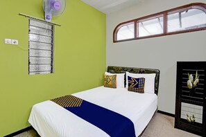 Une pièce comprenant un lit, une fenêtre, un ventilateur fixé au mur et un panneau décoratif orné de motifs floraux.