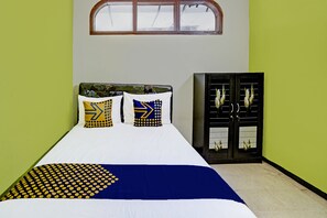 Una cama con colcha blanca y azul, dos almohadas con diseños geométricos y un armario de color oscuro con una ventana.