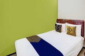 Un lit recouvert d’une couvre-lit blanche et bleue, deux oreillers ornés de motifs géométriques et une tête de lit décorée de motifs floraux.