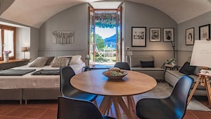 A cozy room with a bed, a dining table with chairs, a small balcony with a view of the mountains, and framed artwork on the walls. - Atelier Dell Artista by Wonderful Italy (Varenna)