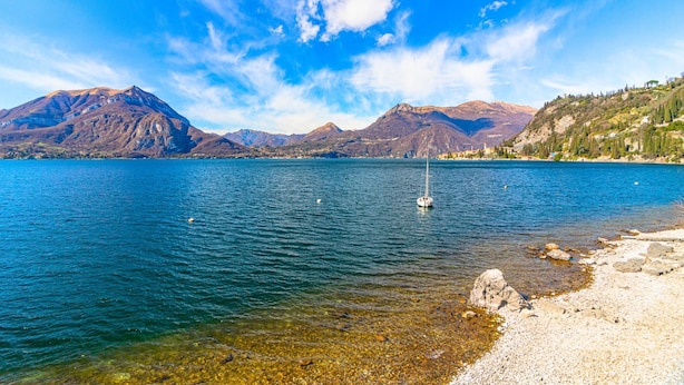 A lake with clear water, a sailboat, and mountains in the background. - Atelier Dell Artista by Wonderful Italy (Varenna)