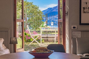 A room with a view of mountains, a table with a bowl of olives, a chair, and a lamp. - Atelier Dell Artista by Wonderful Italy (Varenna)