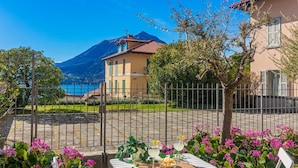 A table set with drinks and snacks, a fenced garden, and a mountain view. - Atelier Dell Artista by Wonderful Italy (Varenna)
