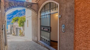 A narrow cobblestone street leading to a building with a metal gate and a mountain view in the background. - Atelier Dell Artista by Wonderful Italy (Varenna)
