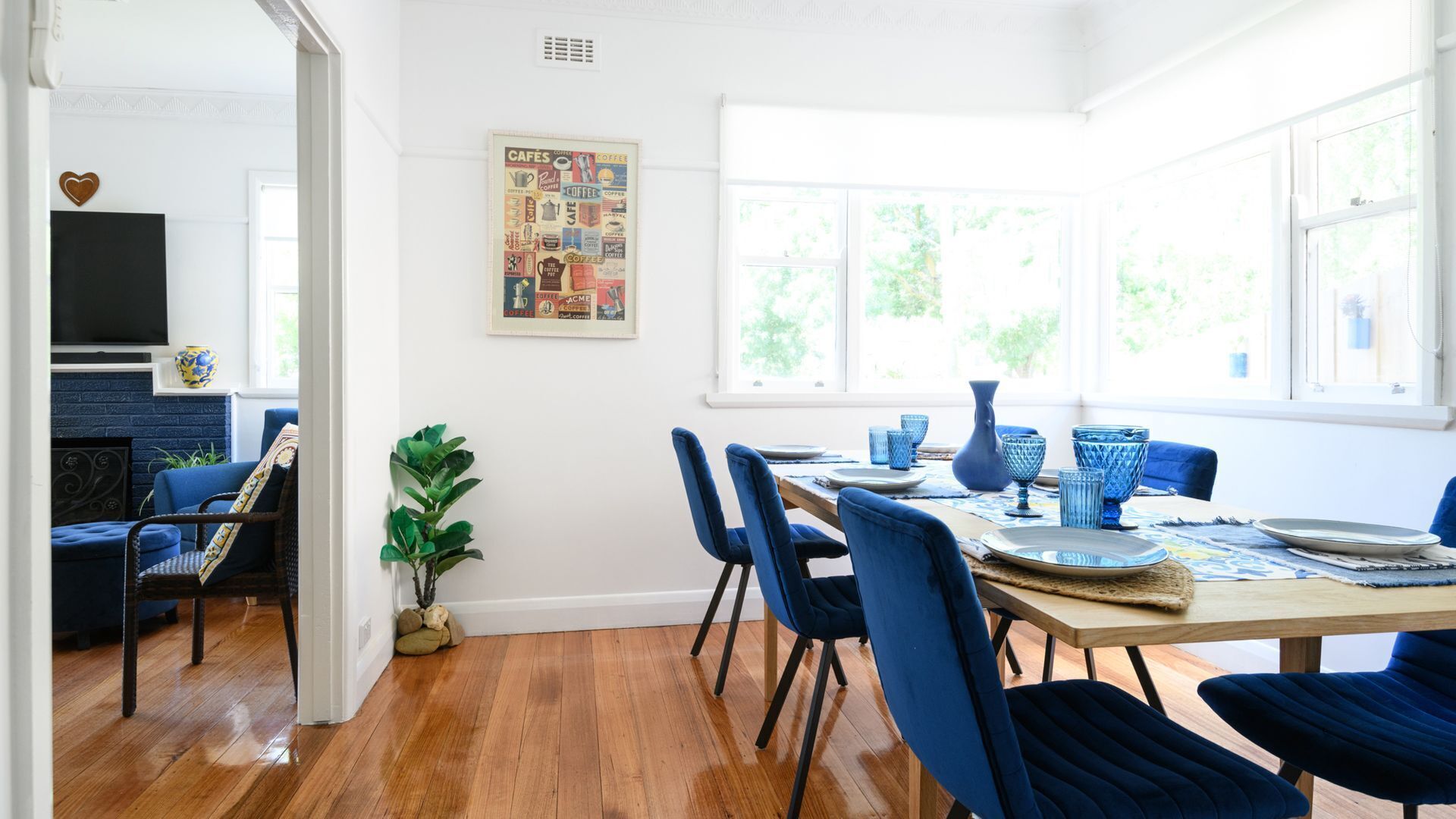 Een eethoek met een houten tafel, blauwe stoelen en wanddecoratie met koffie thema.