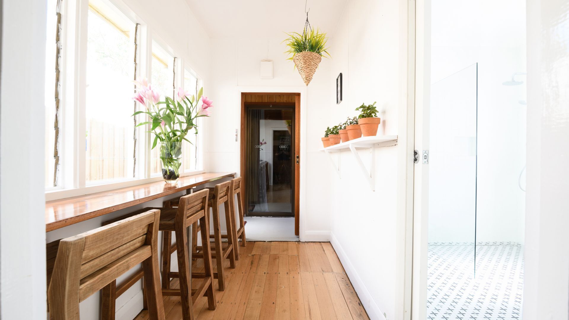 A narrow hallway with wooden flooring, a wooden bench, a potted plant, and a hanging plant.
