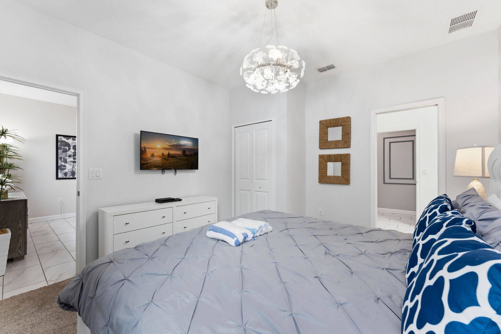 A bedroom with a large bed, a chandelier, a television, and a door.