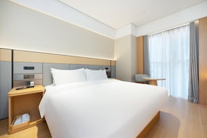 Une chambre d’hôtel moderne avec un grand lit, une table de chevet avec une lampe, une petite table et une fenêtre avec des rideaux.