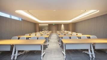 A conference room with rows of tables and chairs, a carpeted floor, and a ceiling with recessed lighting.