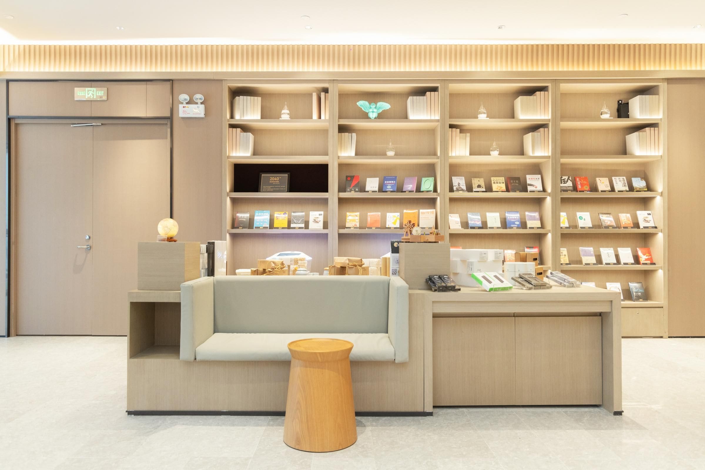 Uma área de recepção moderna com um sofá, um banquinho de madeira e uma estante de livros.