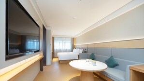 Ein modernes Hotelzimmer mit einem großen Bett, einer Couch, einem runden Tisch und einem an der Wand befestigten Fernseher.