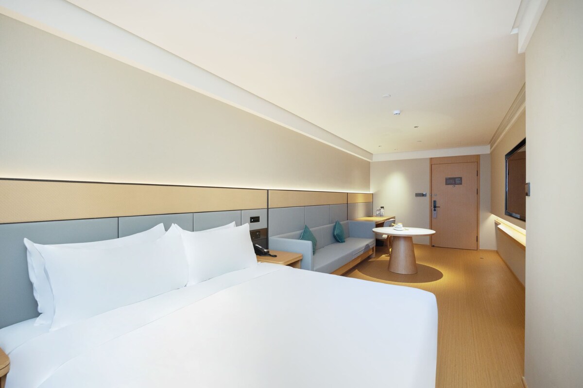 Una habitación de hotel moderna con una cama grande, un sofá, una mesita y un televisor.