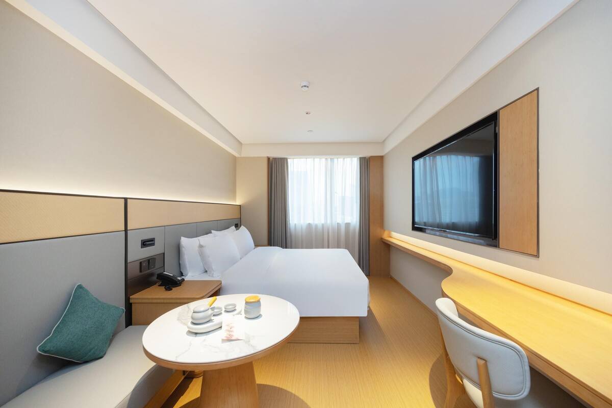 Une chambre d’hôtel moderne, dotée d’un grand lit, d’un bureau, d’une chaise, d’une télévision et d’une fenêtre avec des rideaux.