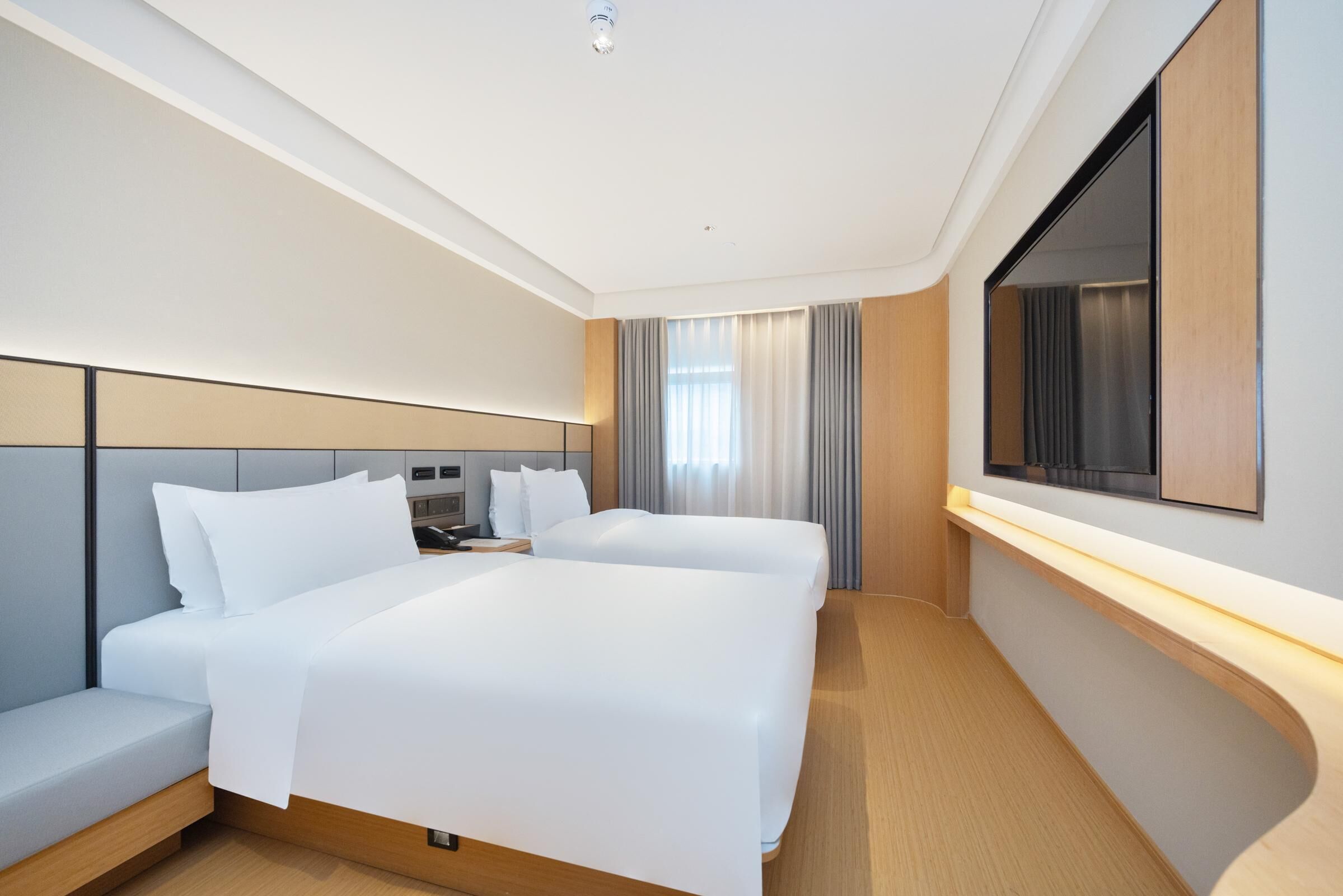 Habitación de hotel moderna con dos camas, un escritorio, un televisor de pantalla plana y un ventanal con cortinas.