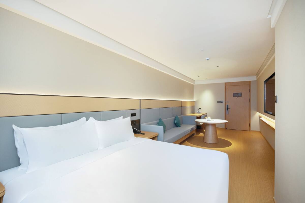 Une chambre d’hôtel moderne avec un grand lit, un canapé, une petite table et un téléviseur.