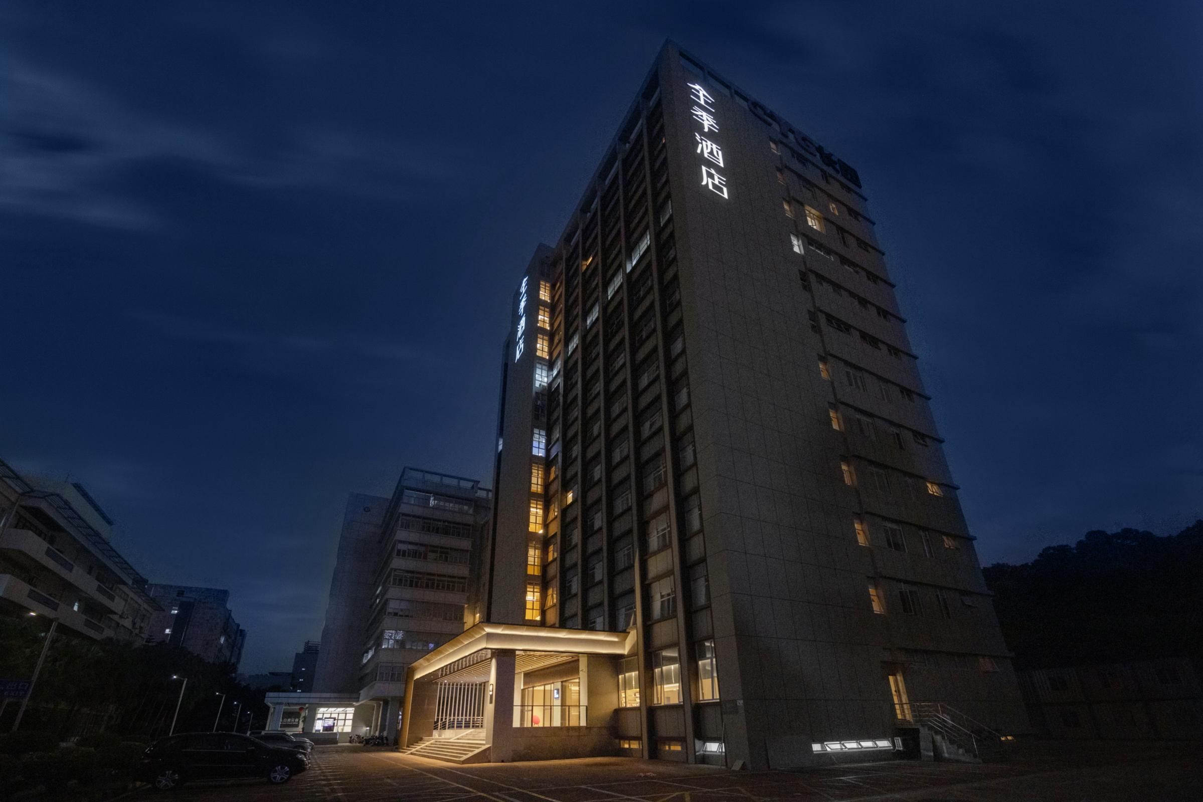 A high-rise hotel building with illuminated signage, a prominent entrance, and a parking area.