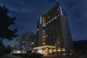 Un edificio de hotel de varios pisos con señalización iluminada y un estacionamiento al frente.