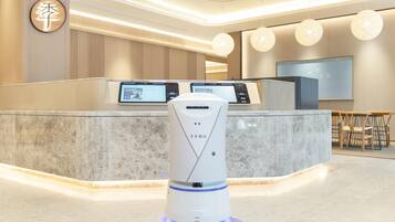 Zona de recepción de hotel con diseño moderno, que incluye un mostrador de recepción con pantallas digitales, un robot y un área de estar con sillones.