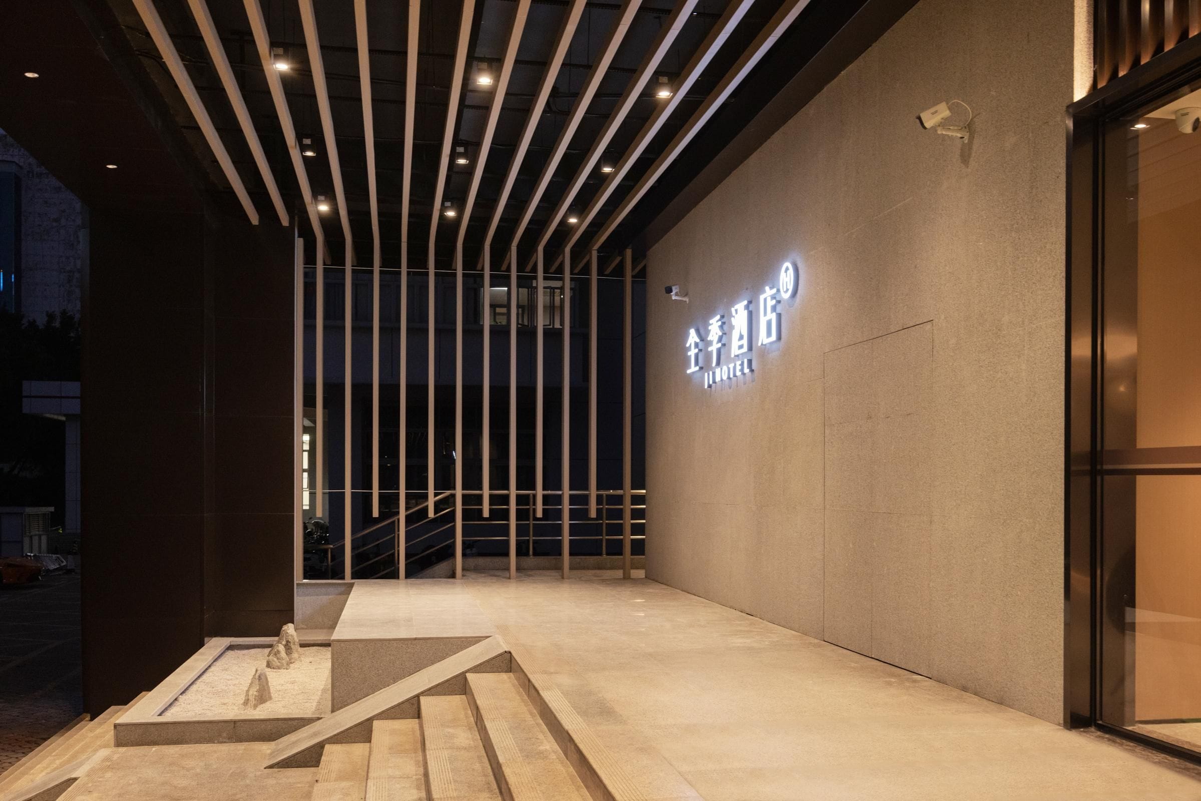 Entrada d'hotel amb disseny modern, que inclou una placa amb el nom de l'hotel, una escala que condueix a l'entrada i una zona d'estar a l'exterior amb un disseny minimalista.