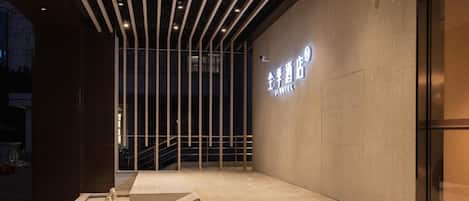 Entrada de hotel con diseño moderno, que incluye un cartel con el nombre del hotel, una escalera que lleva a la entrada y un área de estar exterior minimalista.