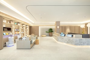A modern hotel lobby with a reception desk, seating area, and shelves with various items. - Ji Hotel Shenzhen Nanshan Technical Park (Shenzhen)