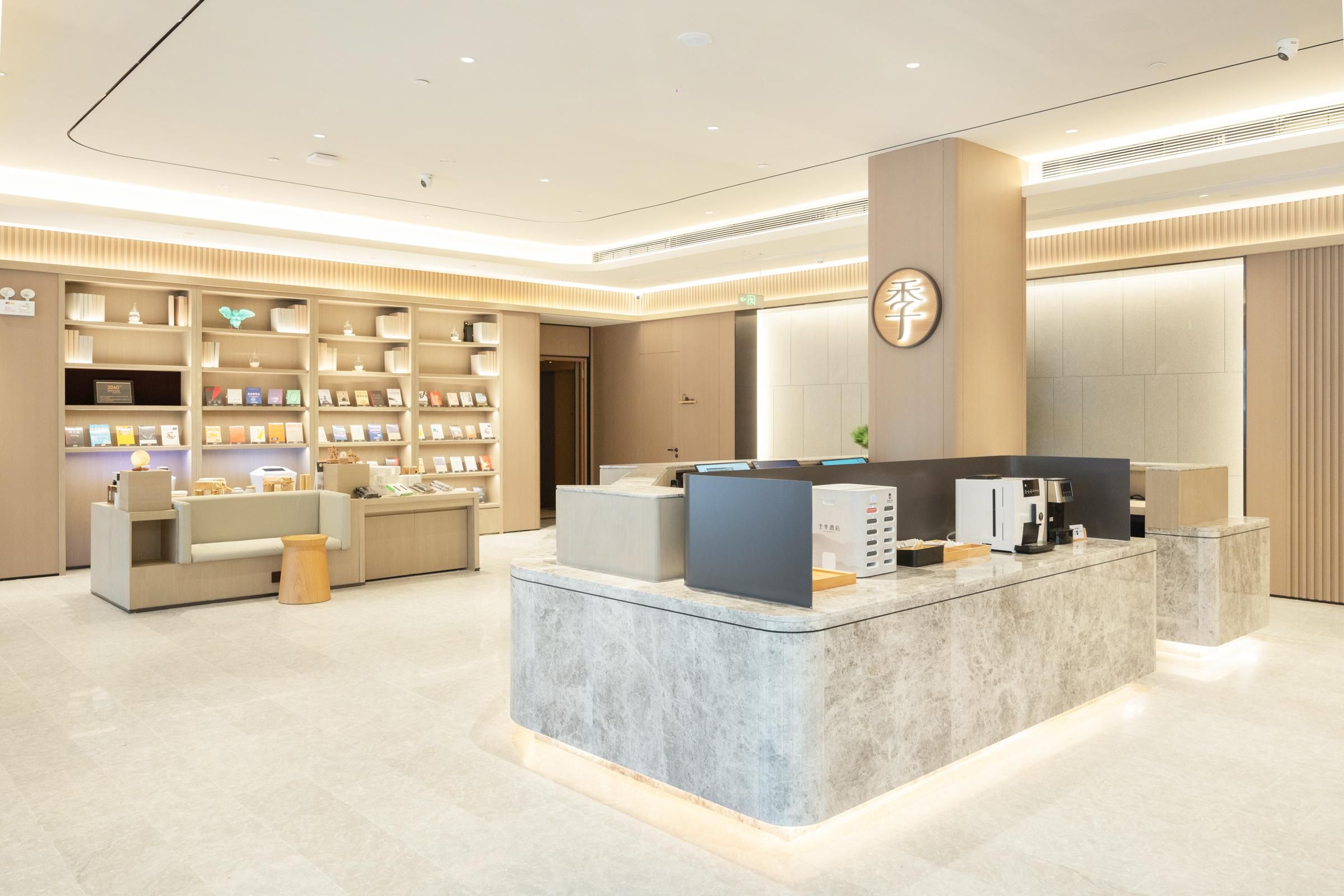 Um hall de hotel moderno com balcão de recepção, área de estar e estantes com livros e revistas.
