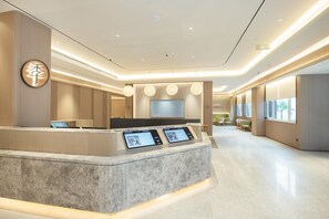 Un espace d’accueil moderne, avec un comptoir en marbre, des écrans numériques et un grand écran de télévision.