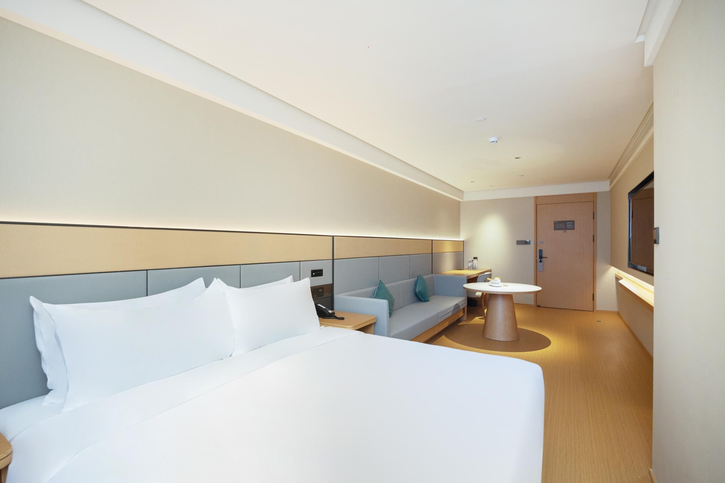 Una habitación de hotel moderna con una cama grande, un sofá, una mesita y un televisor.
