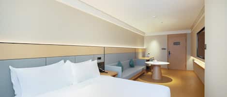 A hotel room with a large bed, a sofa, a small table, and a television.