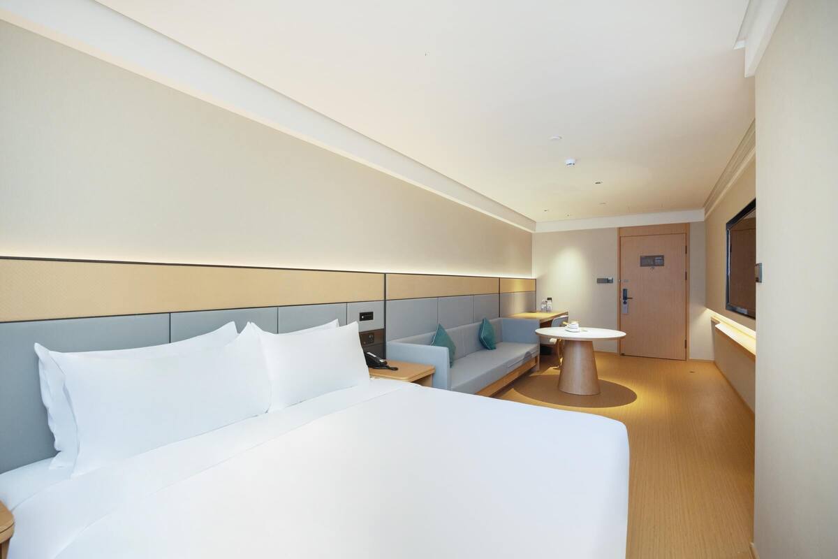 Une chambre d’hôtel moderne avec un grand lit, un canapé, une petite table et un téléviseur.