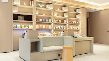 Un área de recepción moderna con un sofá, mesitas de madera y una estantería llena de libros y objetos decorativos.