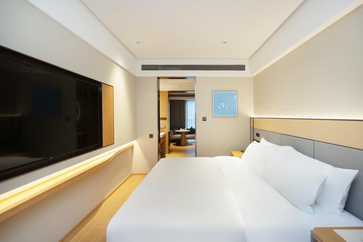 Habitación de hotel con una cama grande, televisión y vista al pasillo.