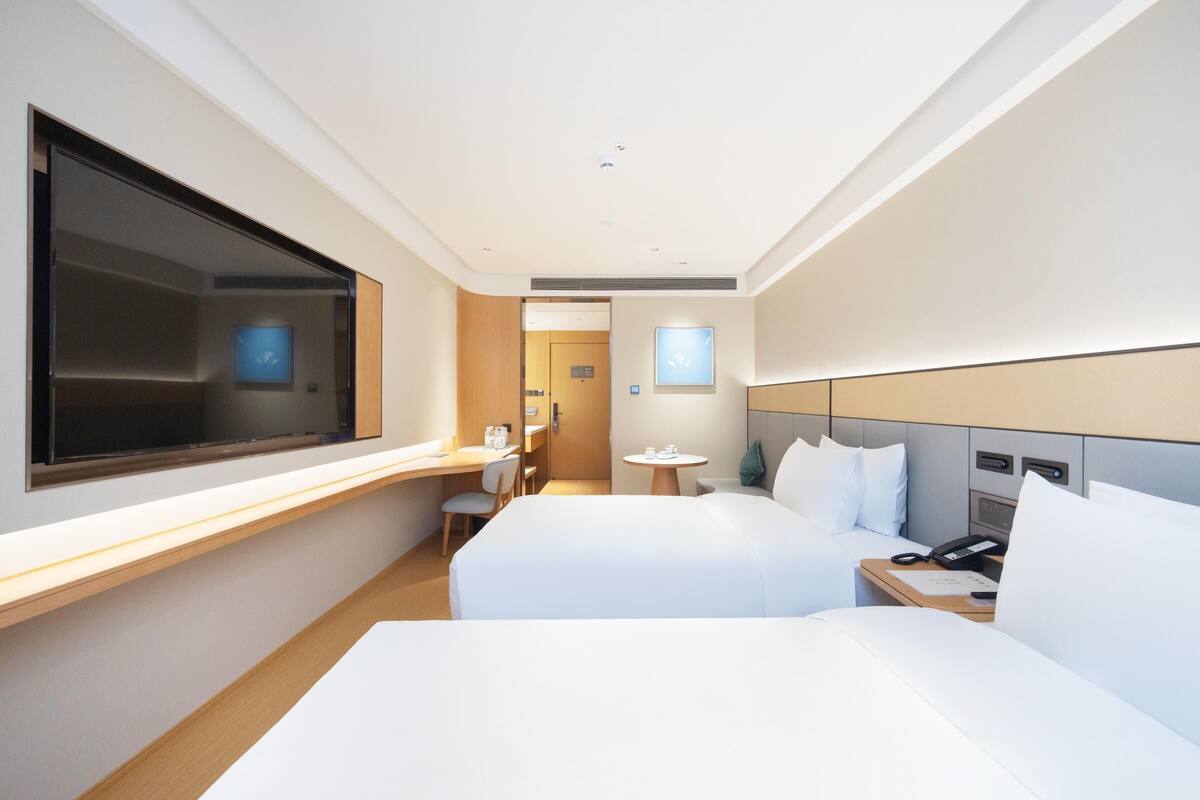 Une chambre d’hôtel moderne équipée de deux lits, d’un bureau, d’une chaise, d’une petite table ronde et d’un téléviseur.