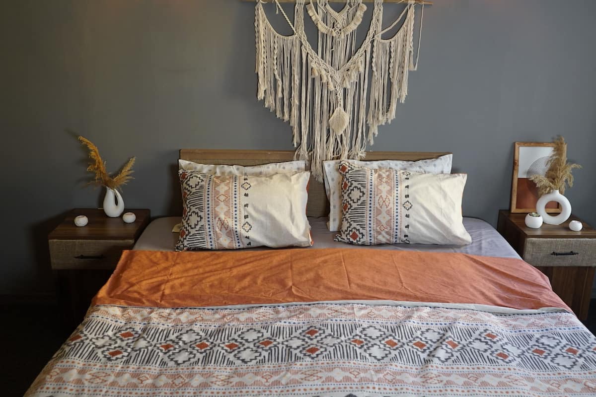 A bed with patterned bedding, two bedside tables with decorative items, and a macrame wall hanging.