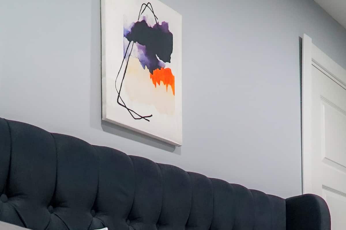 A modern living room with a dark blue tufted sofa, grey and white cushions, and a colorful abstract painting on the wall.