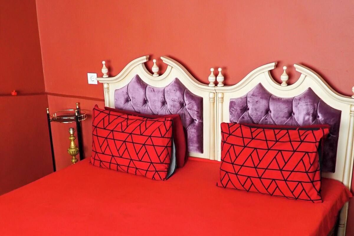 A bed with a red bedspread and two red and black patterned pillows, a wooden headboard, and a red wall.