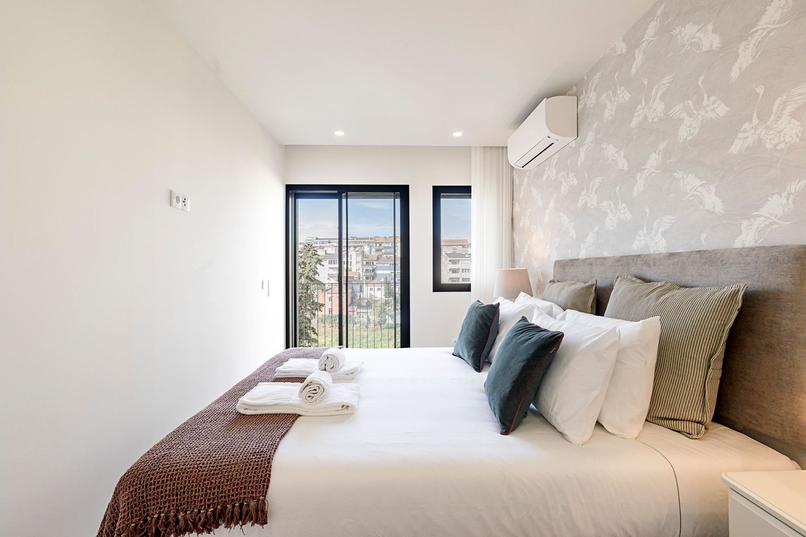Een hotelkamer met een groot bed, uitzicht op de stad en een airconditioner aan de muur.