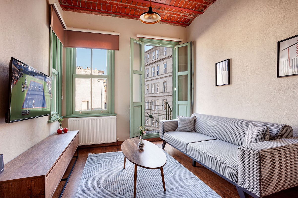 A living room with a sofa, a coffee table, a TV, and a window with green shutters.