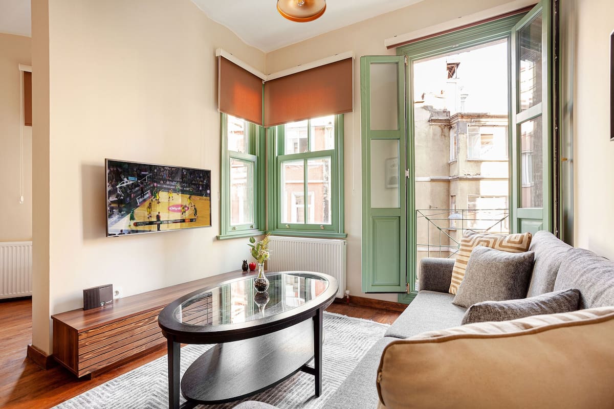 A living room with a glass coffee table, a sofa, and a television displaying a sports event.