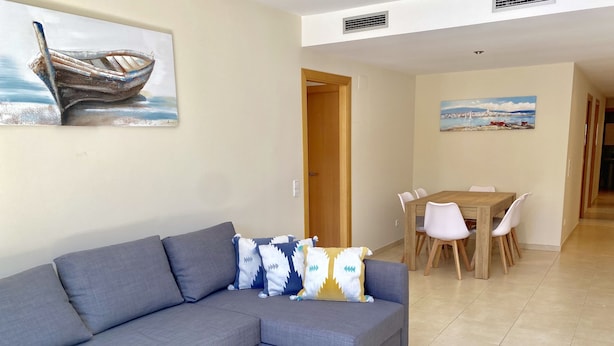 Uma sala de estar com um sofá seccional cinza, uma mesa de jantar com cadeiras e um quadro de um barco na parede.