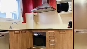 Uma cozinha compacta com armários de madeira, forno embutido, micro-ondas e geladeira de aço inoxidável.