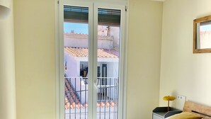 Quarto com cama, mesa de cabeceira, abajur e vista para área externa com varanda.