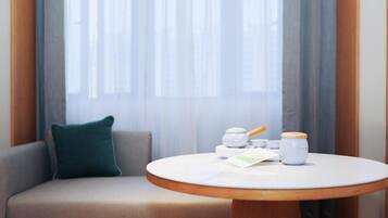 A modern room with a round wooden table, a sofa with a green pillow, and a window with sheer curtains.