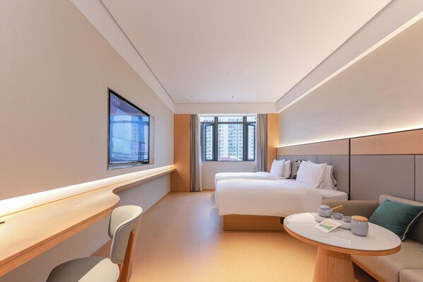 Quarto de hotel com cama, escrivaninha, cadeira, mesa redonda e janela com vista para edifícios.