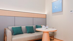 Een moderne kamer met een bank, een rond tafeltje met een theepot, en een ingelijst schilderij aan de muur.