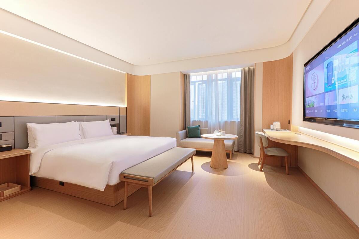 Una habitación de hotel moderna con una cama grande, un escritorio, un sofá y un televisor en la pared.