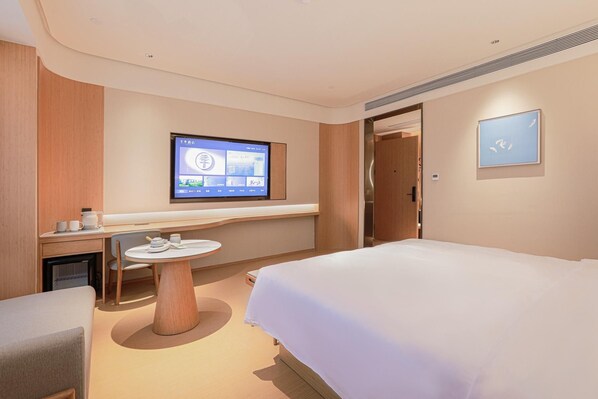A hotel room with a bed, a desk with a computer monitor, a small table with cups, and a door leading to another room. - Ji Hotel Xiamen Xiang'an Maxiang (Xiamen)