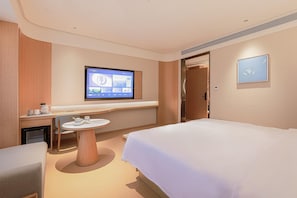 Habitación de hotel con cama, un escritorio con monitor de computadora, una mesita con tazas y una puerta que da a otra habitación.